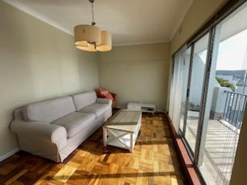 A living room featuring parquet flooring, cove cornicing, and large sliding glass doors that provide access to an outdoor balcony area.