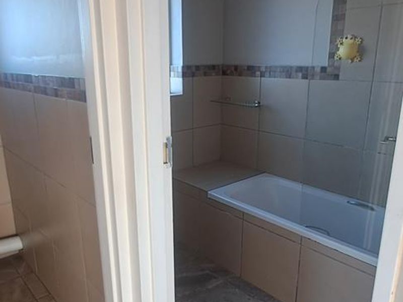 A clean, neutral-toned bathroom featuring a built-in bathtub with tiled surround and a glass shower screen.