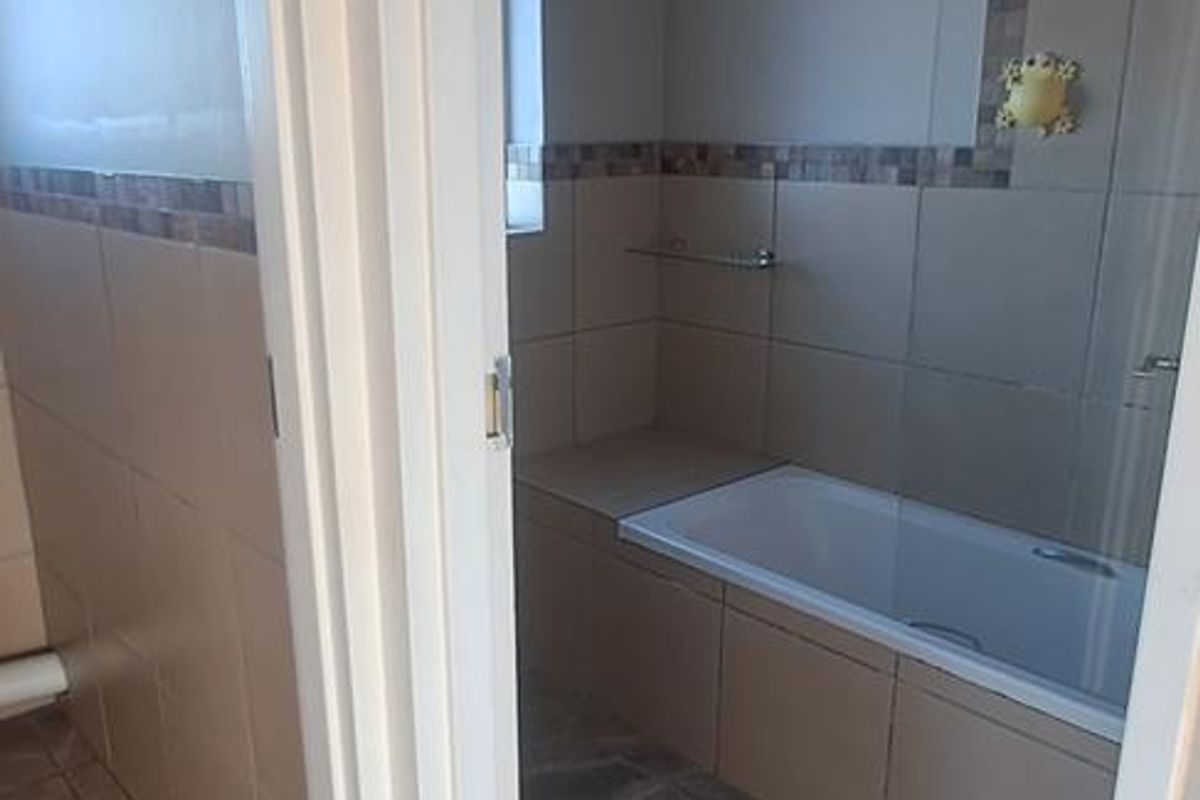 A clean, neutral-toned bathroom featuring a built-in bathtub with tiled surround and a glass shower screen.
