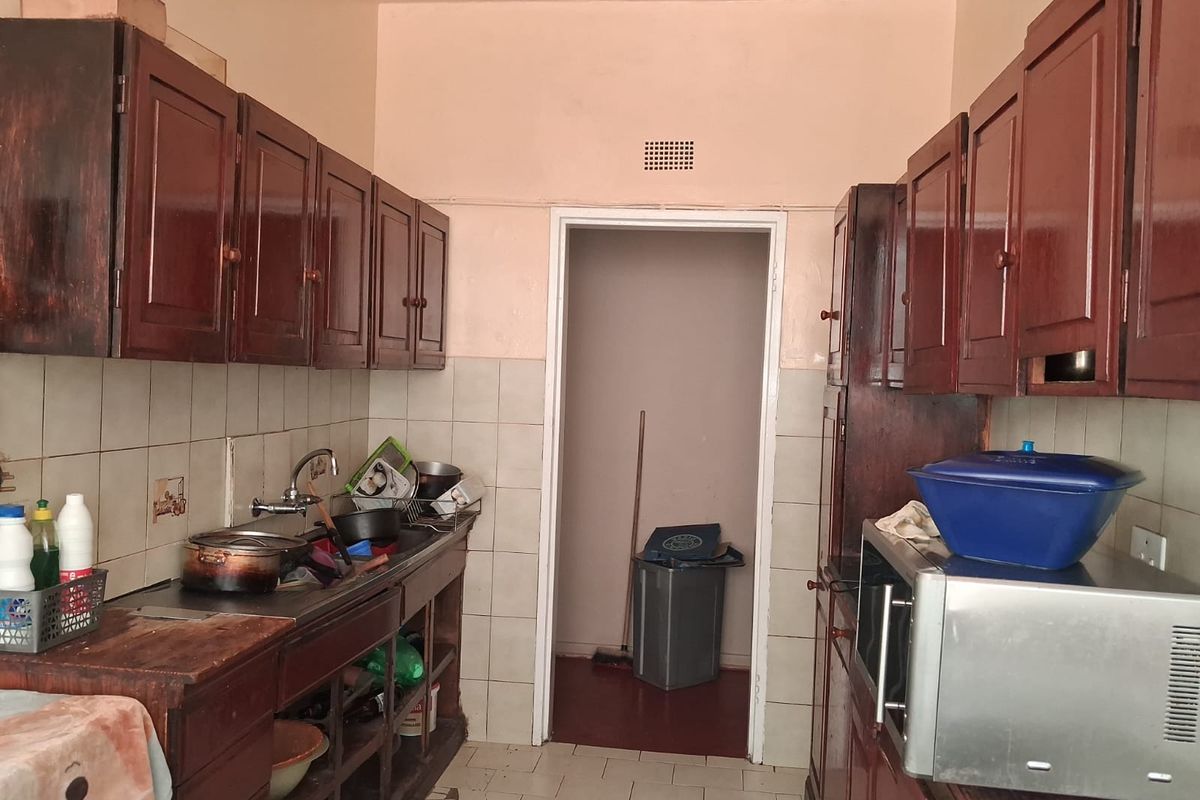 A dated kitchen featuring dark wooden cabinetry, a stainless steel sink, and tiled finishes, offering significant potential for modernization and renovation.