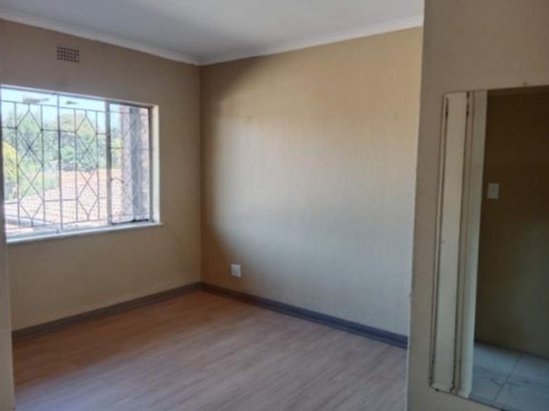 An empty bedroom featuring laminate flooring, a window with security bars, and a built-in mirror, offering a blank canvas for personalization.