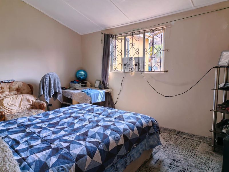 A bedroom featuring a window with security bars and visible wall surface wear, requiring cosmetic updates to improve the overall aesthetic.