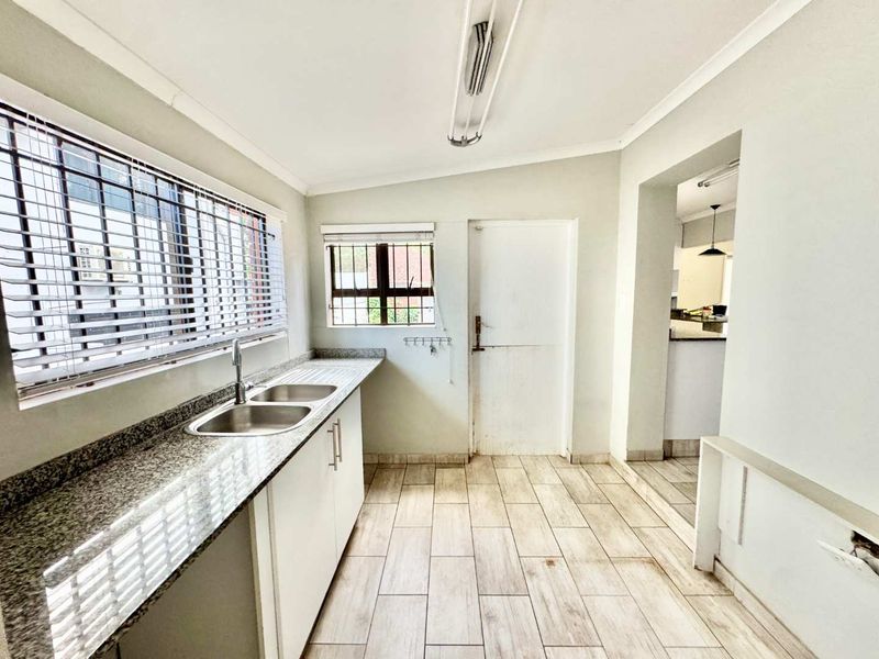 A functional scullery area featuring granite countertops, a double basin sink, and tiled flooring, providing a practical space for kitchen preparation and utility tasks.