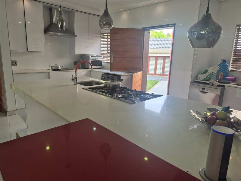 Modern kitchen featuring a large central island with gas hob, stone countertops, high-gloss cabinetry, and direct access to the outdoor area.