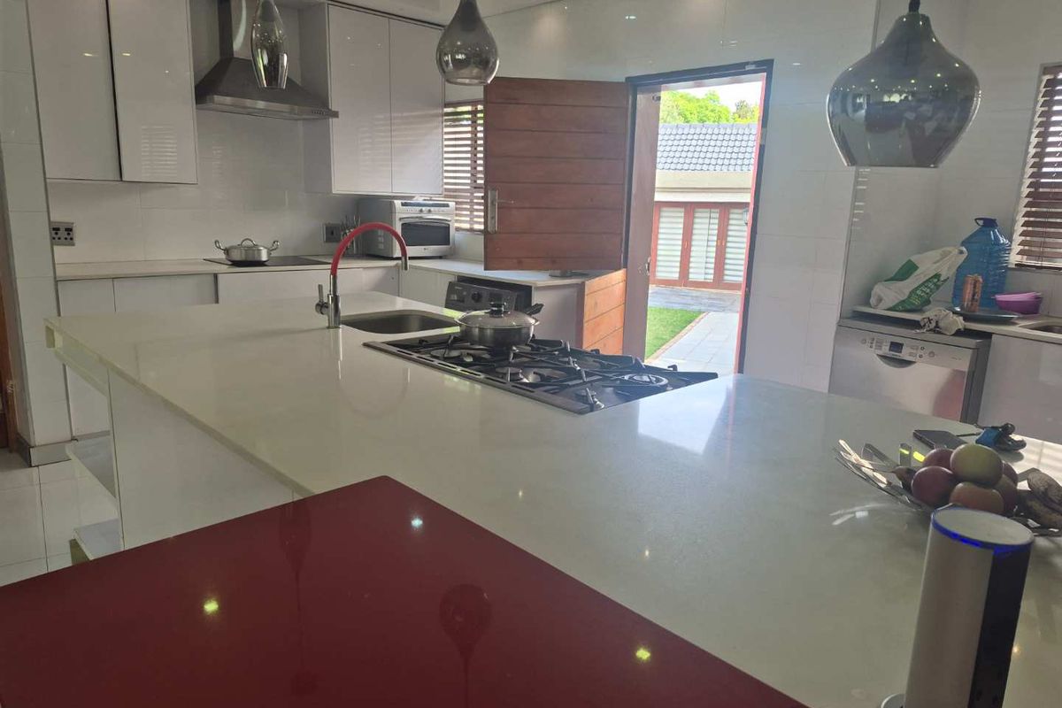 Modern kitchen featuring a large central island with gas hob, stone countertops, high-gloss cabinetry, and direct access to the outdoor area.