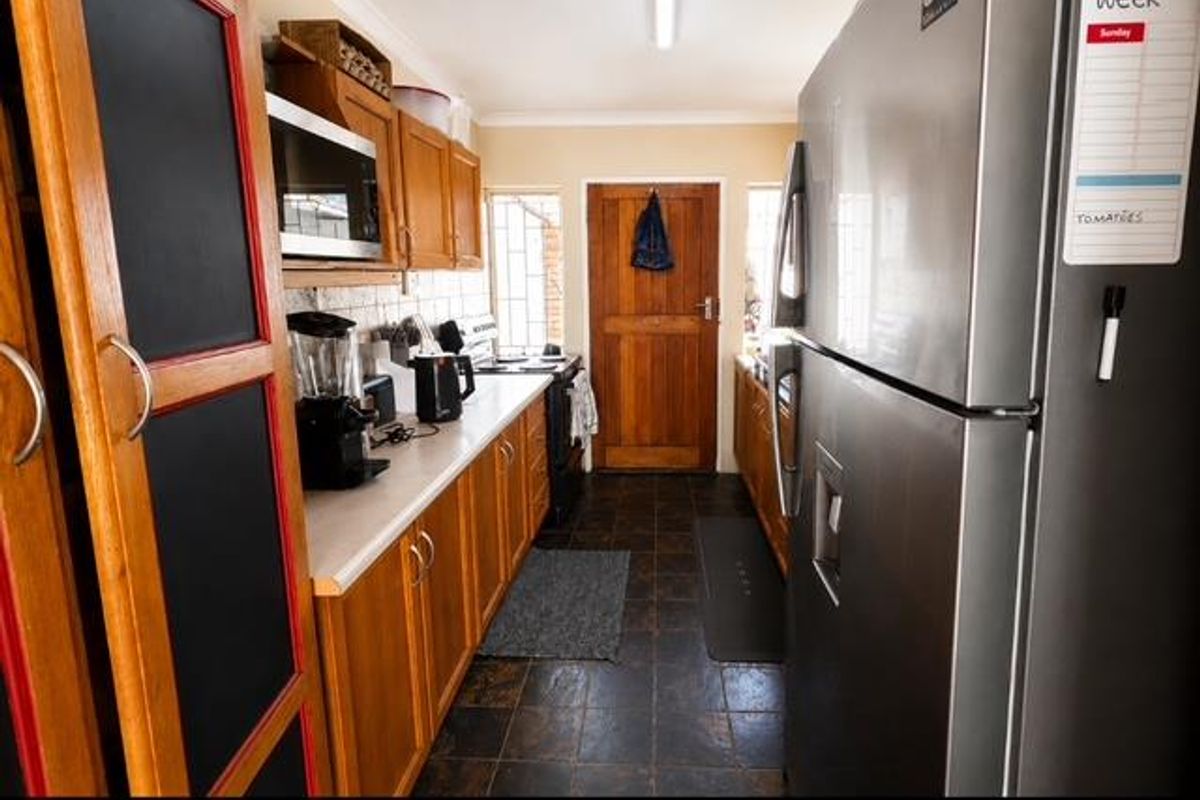 A functional galley-style kitchen featuring wooden cabinetry, laminate countertops, and tiled flooring, providing a practical workspace with direct access to the exterior.