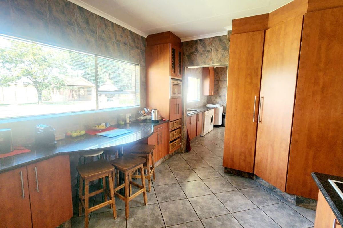 Spacious kitchen featuring extensive wooden cabinetry, granite countertops, and tiled finishes, with an adjoining scullery area visible through the doorway.