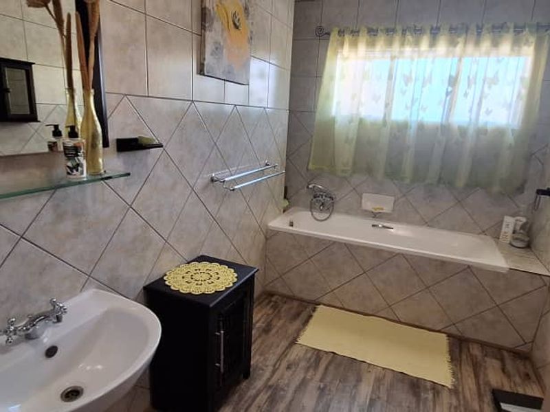 A functional bathroom featuring a built-in bathtub, wall-mounted basin, and tiled wall finishes throughout.