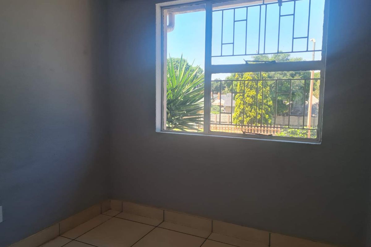 An empty bedroom featuring tiled flooring, a window with security bars, and a curtain rail, offering a blank canvas for personalization.