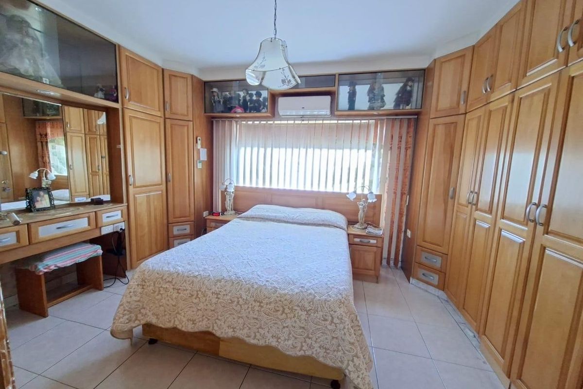 A bedroom featuring extensive built-in wooden cabinetry, a matching vanity unit, tiled flooring, and a wall-mounted air conditioning unit.