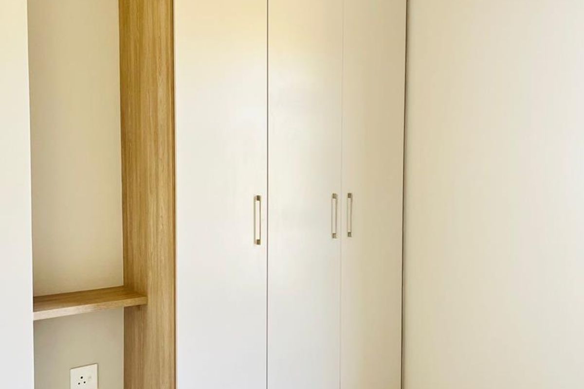 A bedroom featuring modern, built-in floor-to-ceiling cabinetry with a light wood finish and integrated shelving, complemented by neutral tiled flooring.