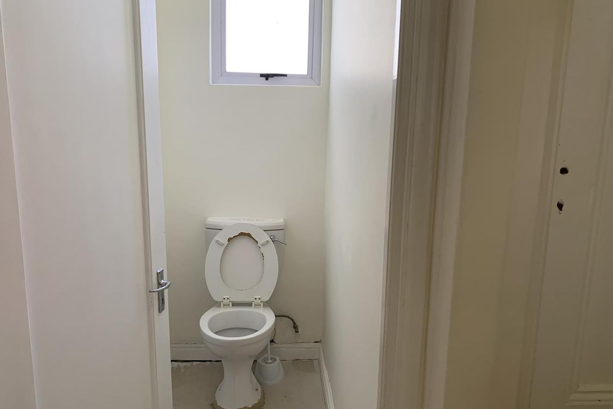 A small, functional office restroom featuring a standard toilet and a small window, currently requiring maintenance and cosmetic updates.