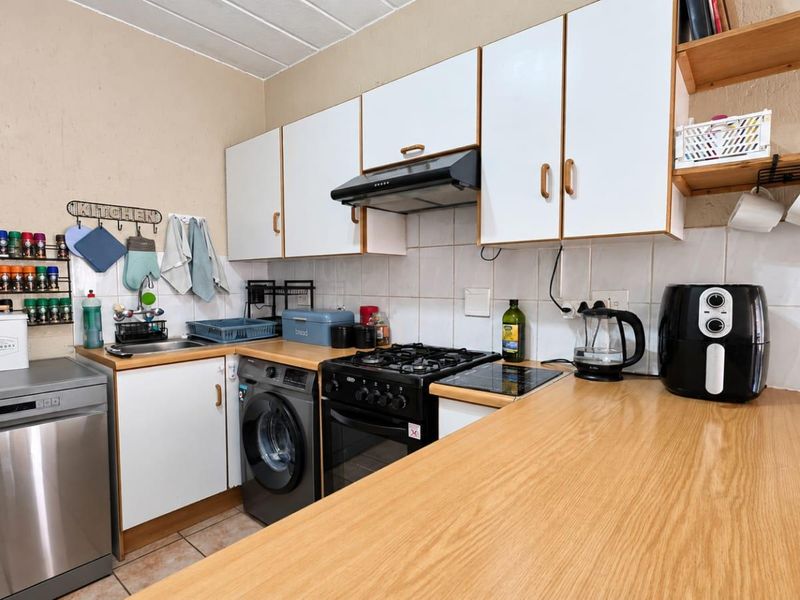 A functional kitchen featuring built-in cabinetry, a gas stove with extractor fan, laminate countertops, and tiled backsplash with integrated appliance space.