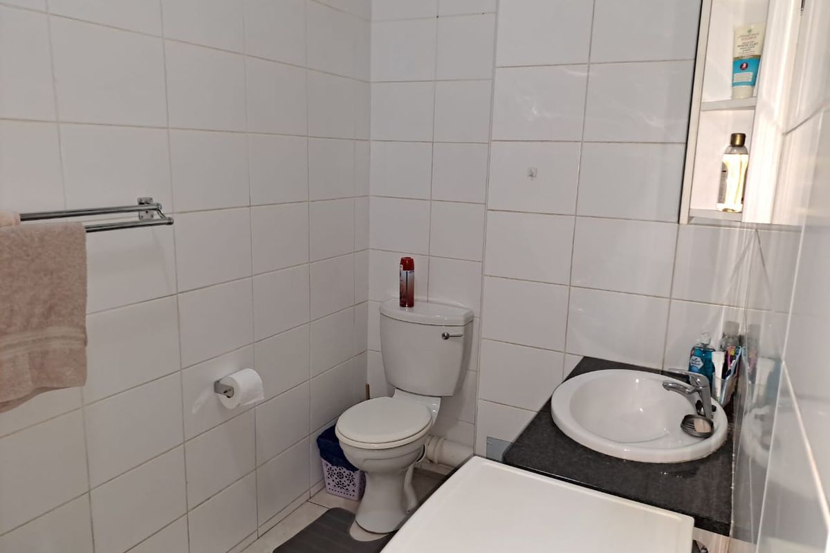 A functional bathroom featuring white wall tiles, a pedestal toilet, a vanity with a drop-in sink, and a built-in medicine cabinet.