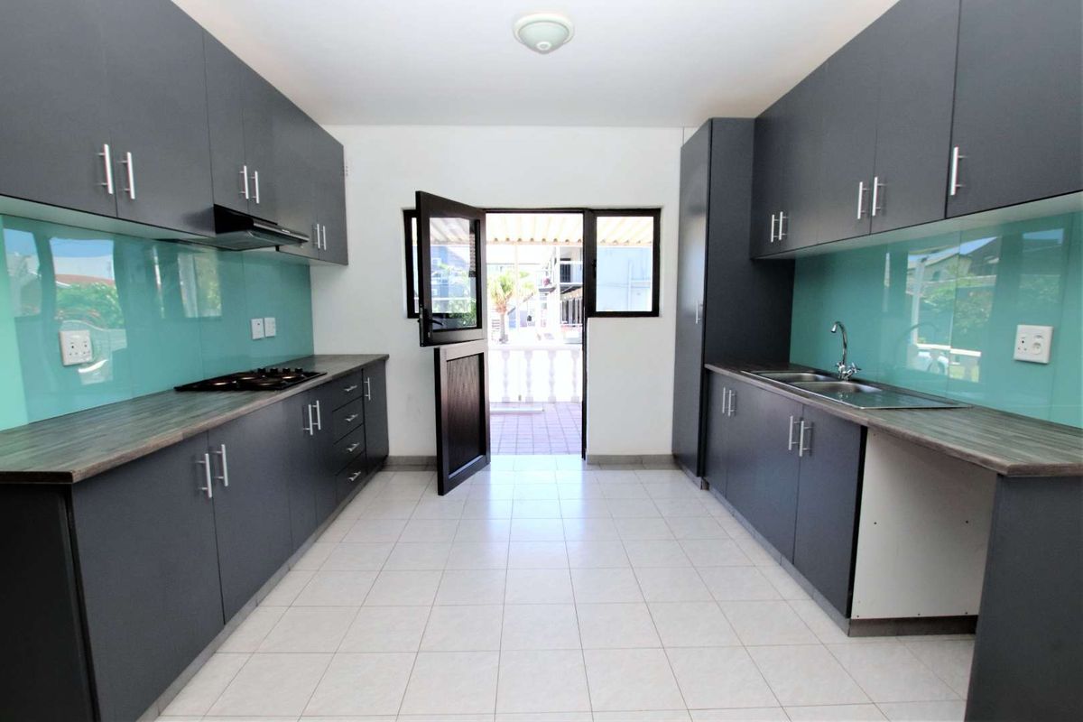 Modern galley-style kitchen featuring dark grey cabinetry, glass splashbacks, gas hob, extractor fan, and direct access to an outdoor patio area.