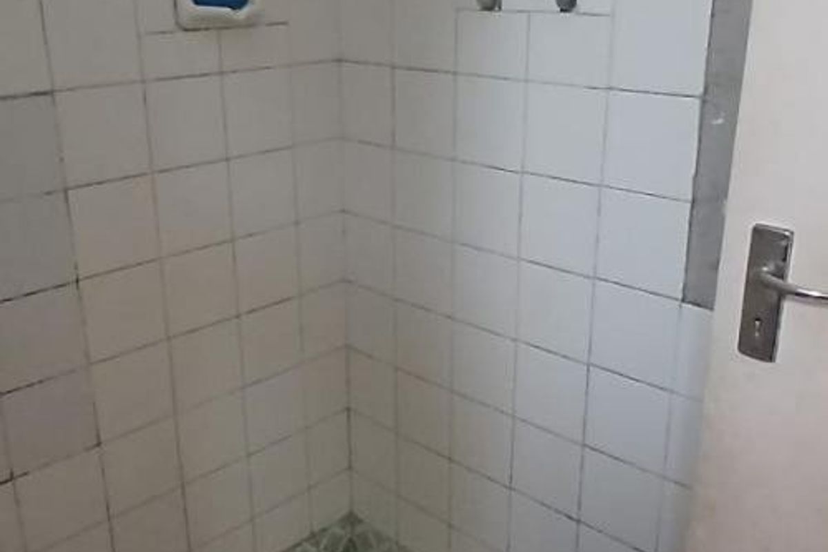 A functional shower enclosure featuring white wall tiles, a standard shower mixer, and a built-in soap recess, requiring cosmetic updates to improve its condition.