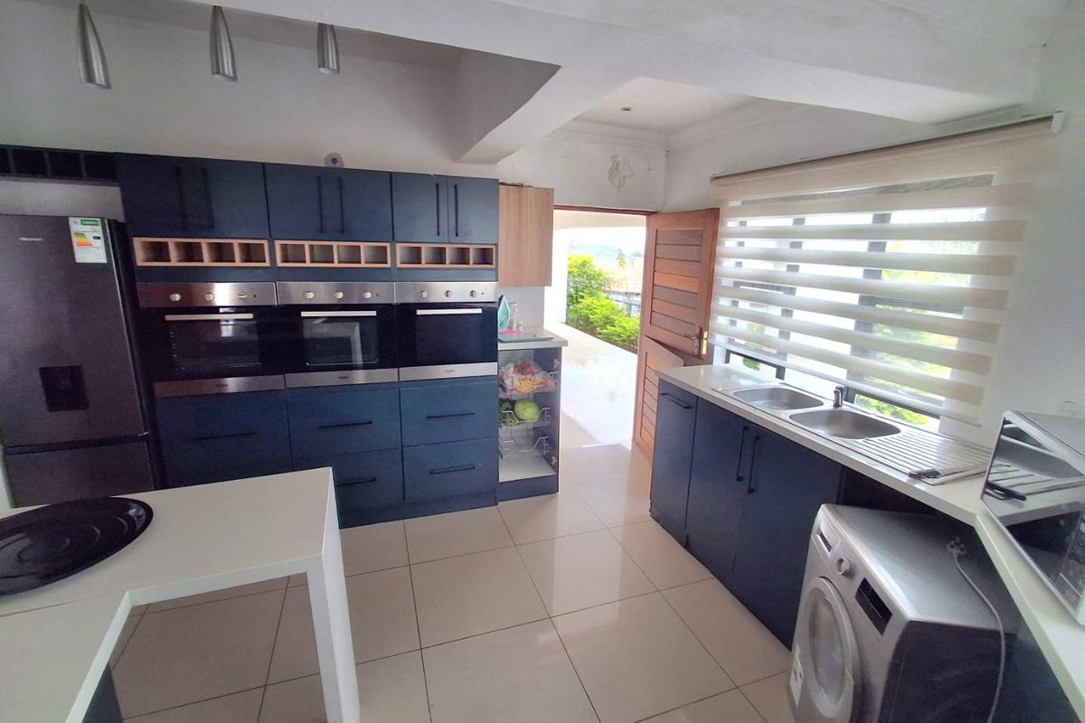 Modern kitchen featuring dark blue cabinetry, built-in triple ovens, double sink, and tiled flooring with direct access to an outdoor area.