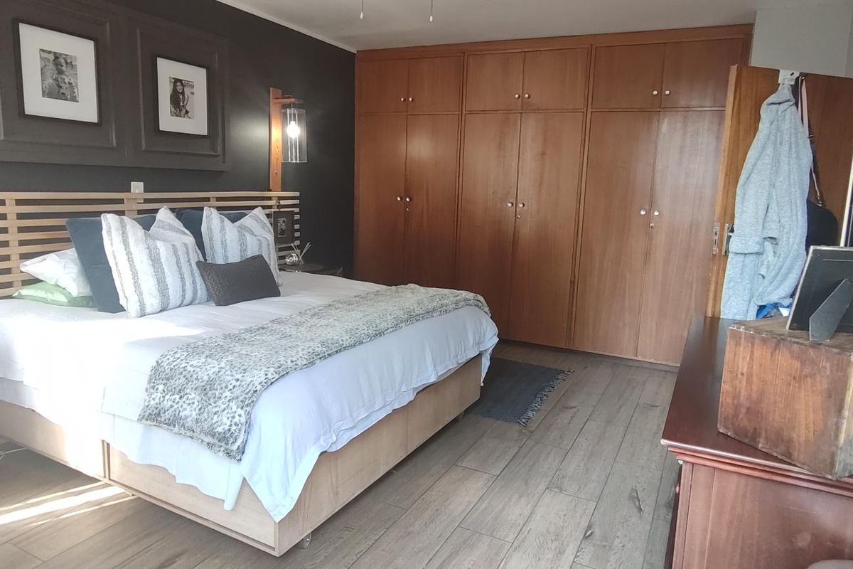 Spacious bedroom featuring extensive built-in wooden cupboards, modern laminate flooring, and dark accent wall detailing.