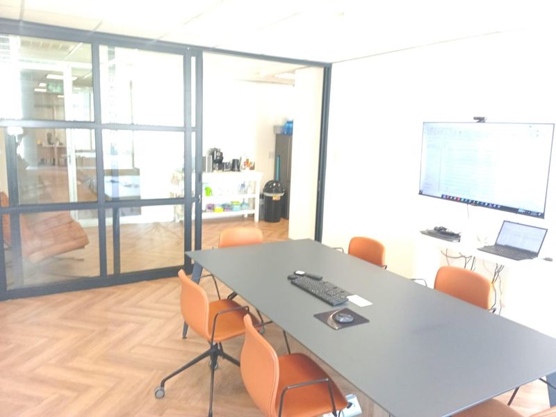 A modern office meeting room featuring herringbone flooring, a black metal-framed glass partition, and a suspended ceiling.