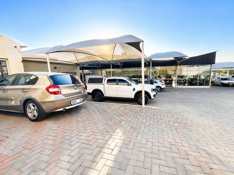 Exterior view of a retail property featuring a paved parking area with shade cloth structures and large glass storefront windows.