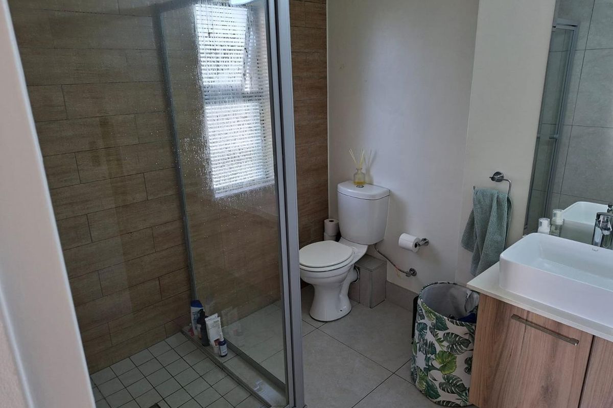 A modern bathroom featuring a glass-enclosed shower, wood-look wall tiling, a vanity with a vessel sink, and neutral floor tiles.