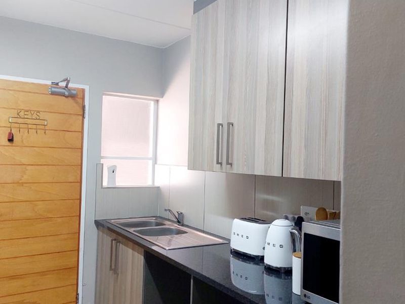 A compact, modern kitchen featuring laminate cabinetry, granite countertops, a stainless steel sink, and tiled flooring, providing a functional and clean workspace.