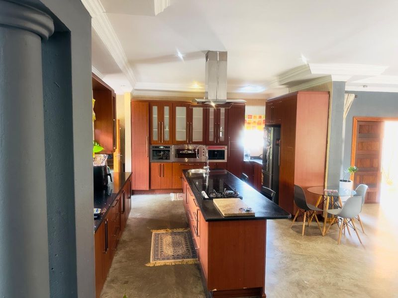 Spacious kitchen featuring dark wood cabinetry, a central island with a built-in hob, stainless steel extractor fan, and integrated oven units.