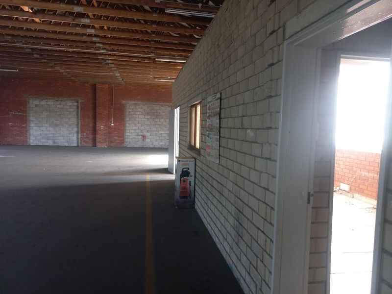 Spacious industrial utility area featuring exposed timber roof trusses, brick walls, and concrete flooring, suitable for storage or workshop use.