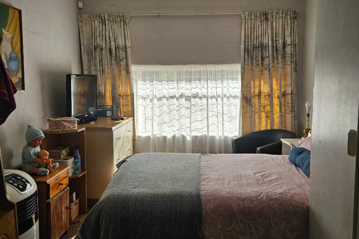 A functional bedroom featuring tiled flooring, a large window with curtains, and built-in storage space.