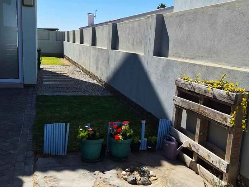 A rear exterior area featuring a concrete patio, a small lawn section, and a long boundary wall, providing a private outdoor space.