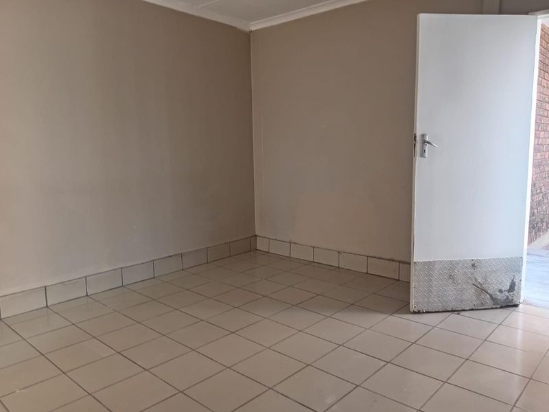 An empty bedroom featuring neutral tiled flooring and a door with a protective metal kickplate.