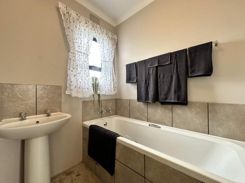 A functional bathroom featuring a pedestal basin and a tiled built-in bathtub with neutral wall finishes.