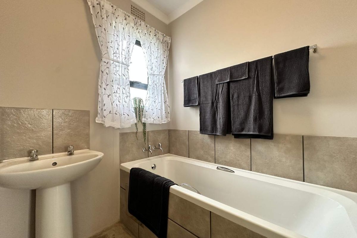 A functional bathroom featuring a pedestal basin and a tiled built-in bathtub with neutral wall finishes.