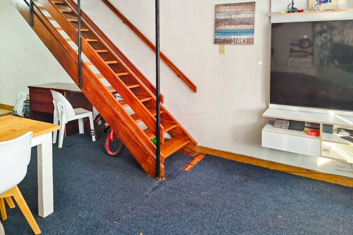 Living area featuring a wooden staircase and wall-mounted shelving unit, requiring cosmetic updates to the flooring and wall finishes.