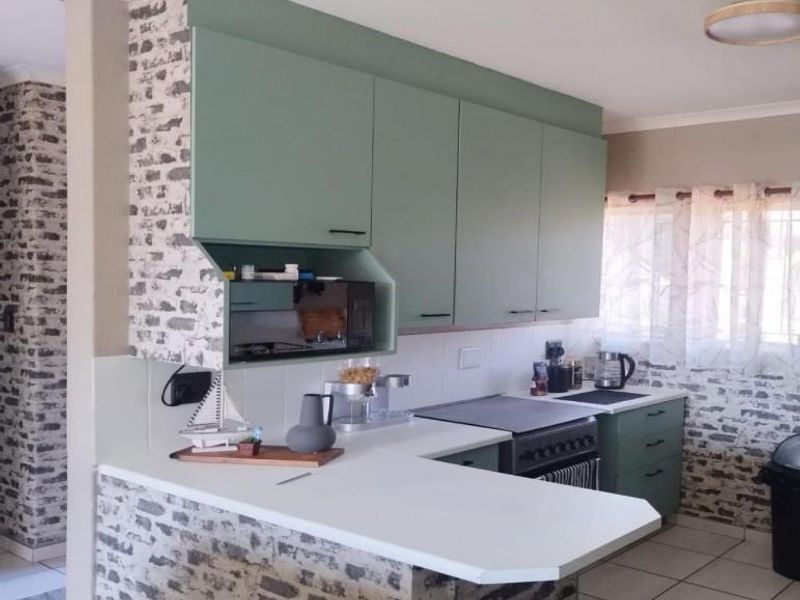 A functional kitchen featuring sage green cabinetry, white countertops, a built-in microwave nook, and a tiled backsplash with decorative brick-patterned wall finishes.