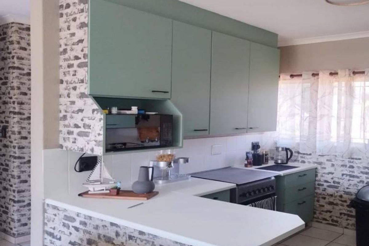 A functional kitchen featuring sage green cabinetry, white countertops, a built-in microwave nook, and a tiled backsplash with decorative brick-patterned wall finishes.