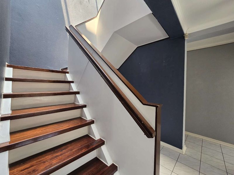 A bright hallway featuring a wooden staircase with a matching handrail and tiled flooring, leading to an open transition area.