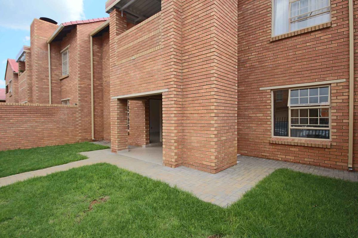 Rear view of the apartment building featuring a face brick facade, a private paved patio area, and a small maintained lawn.