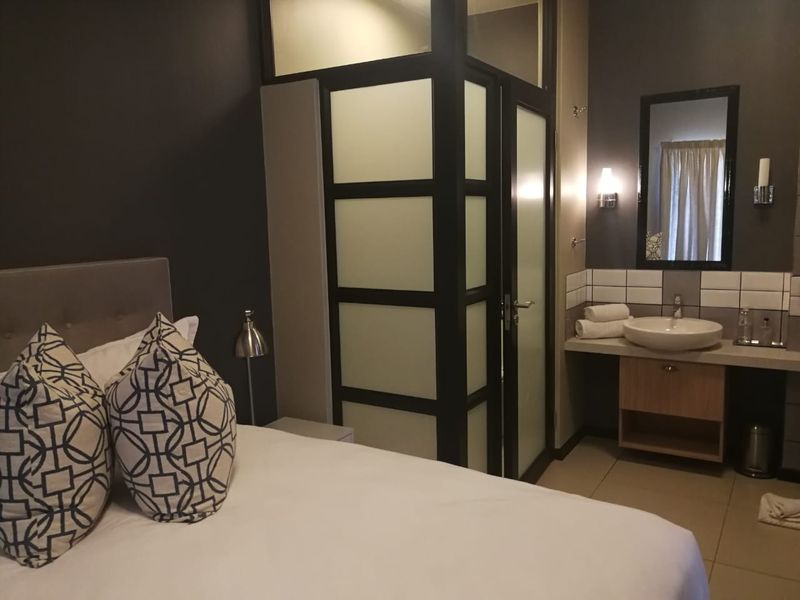 A modern bedroom featuring an integrated en-suite bathroom with a frosted glass partition, vessel sink, and vanity cabinet.
