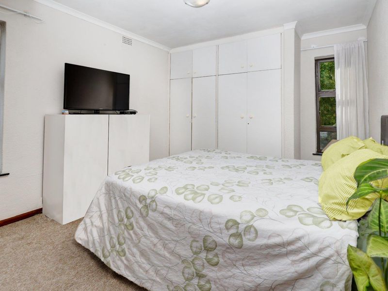 A functional bedroom featuring built-in cupboards, carpeted flooring, and natural light from casement windows.