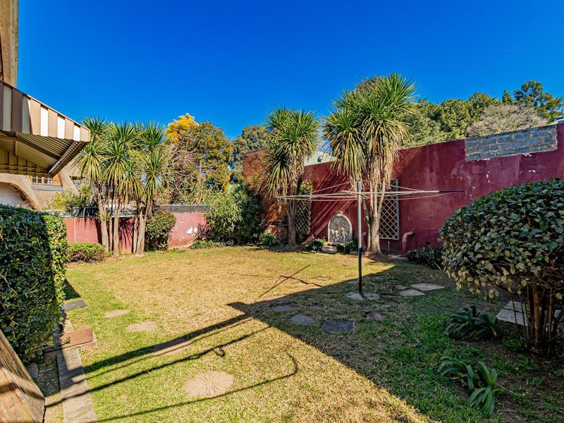 A private rear garden featuring a lawn, mature trees, and a boundary wall with visible maintenance requirements.