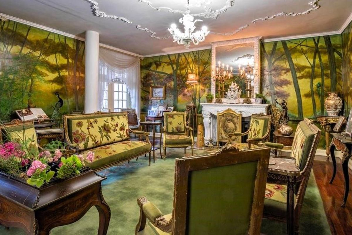 A formal living room featuring ornate ceiling molding, a classic fireplace mantel, and hardwood flooring, decorated with a distinctive mural wall finish.