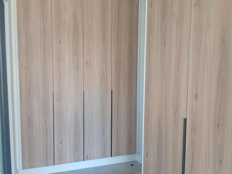 A clean hallway featuring modern light wood-finish built-in cupboards and neutral floor tiles.