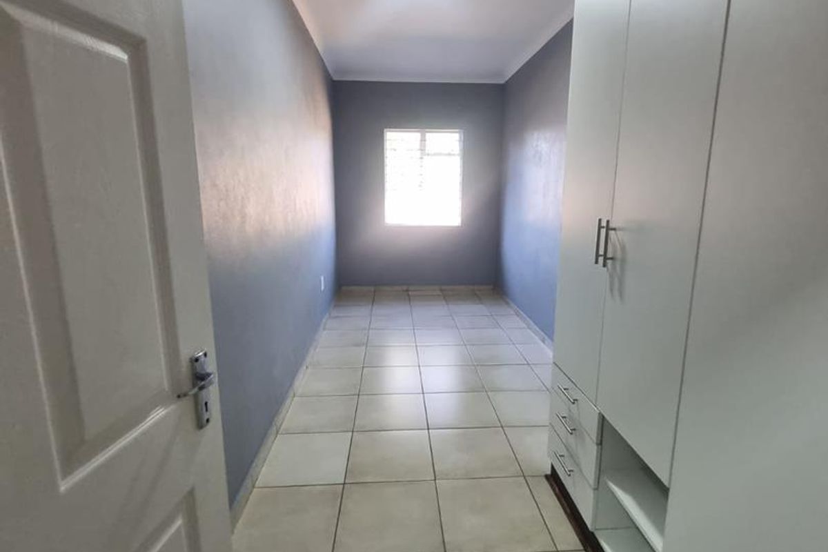 A clean, empty bedroom featuring neutral tiled flooring, dark accent walls, and ample built-in cupboard storage space.