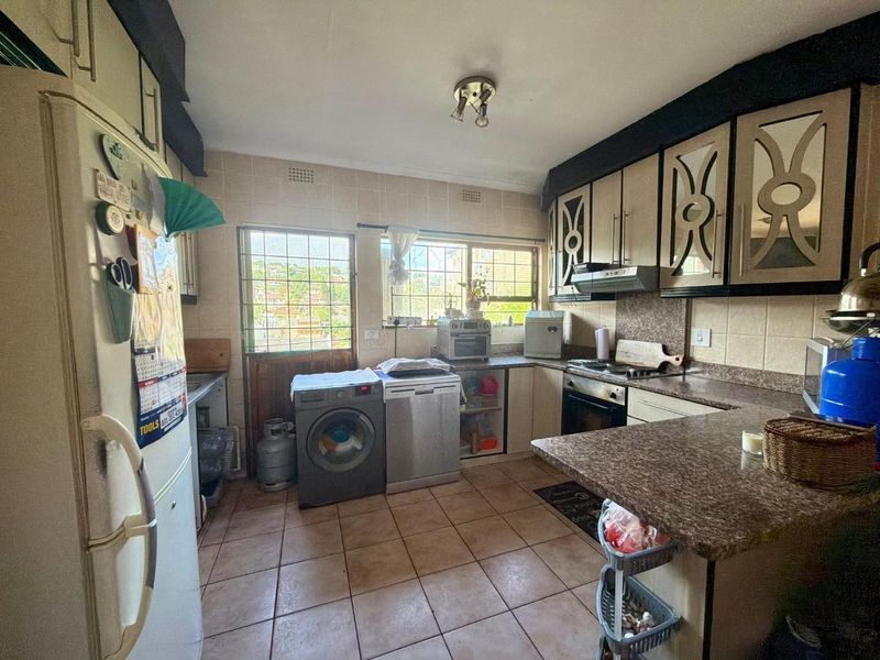 Functional kitchen featuring tiled flooring, built-in cabinetry, laminate countertops, and integrated cooking appliances, with direct access to an exterior security door.