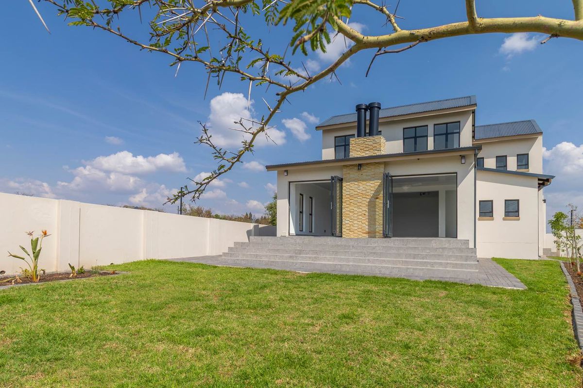 Rear view of a modern double-story house featuring a stone-clad chimney, concrete patio steps, and bi-fold doors leading to a landscaped garden.