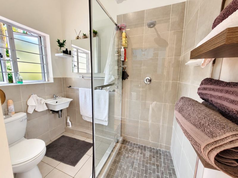 A modern bathroom featuring a glass-enclosed shower with tiled walls, a wall-mounted basin, and a standard toilet, finished with neutral ceramic tiling.
