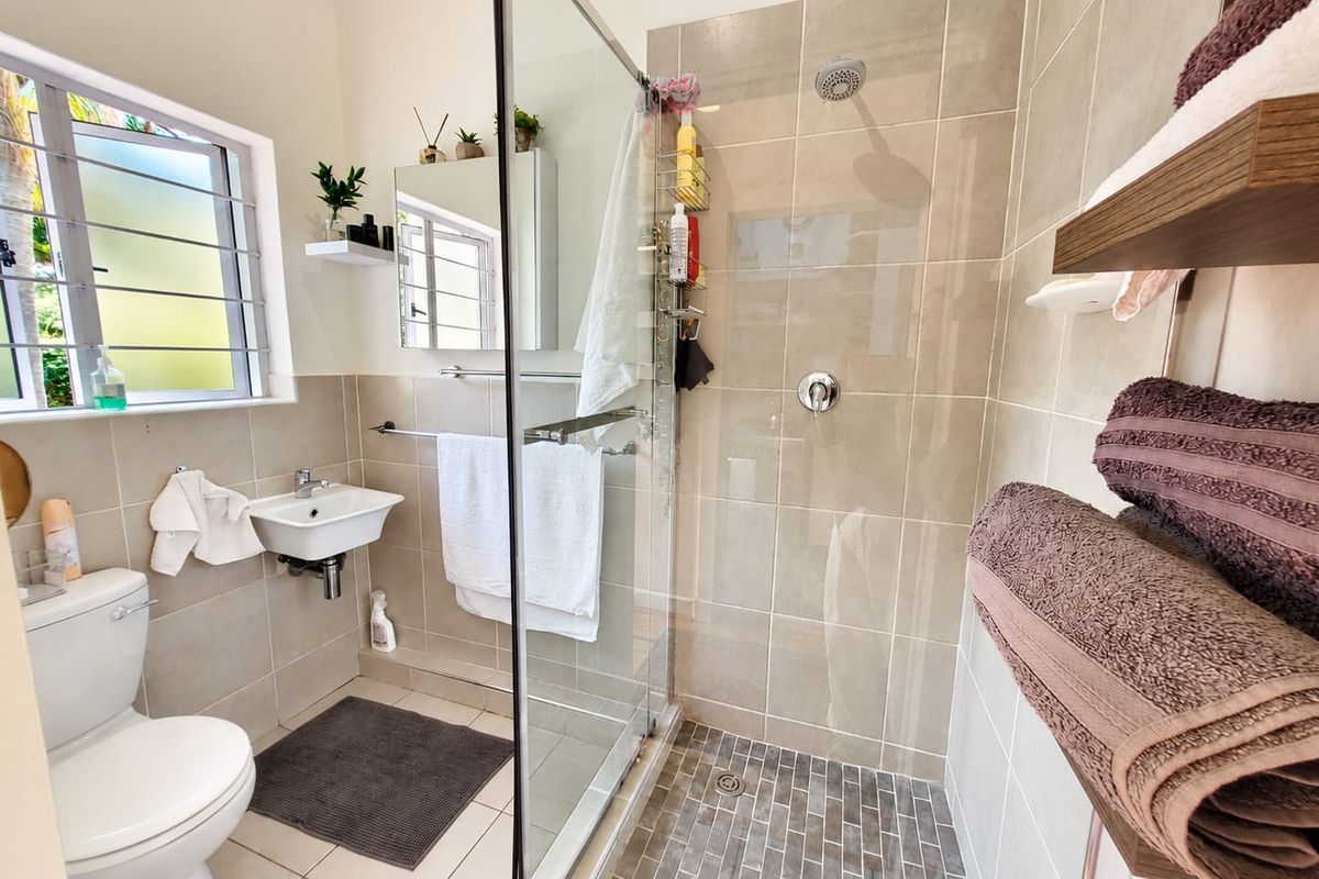 A modern bathroom featuring a glass-enclosed shower with tiled walls, a wall-mounted basin, and a standard toilet, finished with neutral ceramic tiling.