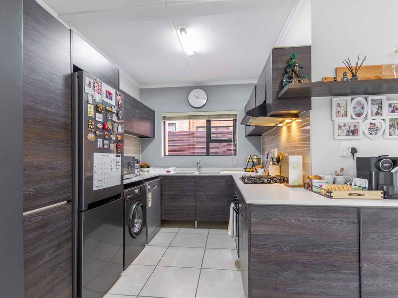 Modern kitchen featuring dark wood-grain cabinetry, light countertops, tiled flooring, a gas hob, and an integrated extractor fan with under-cabinet lighting.