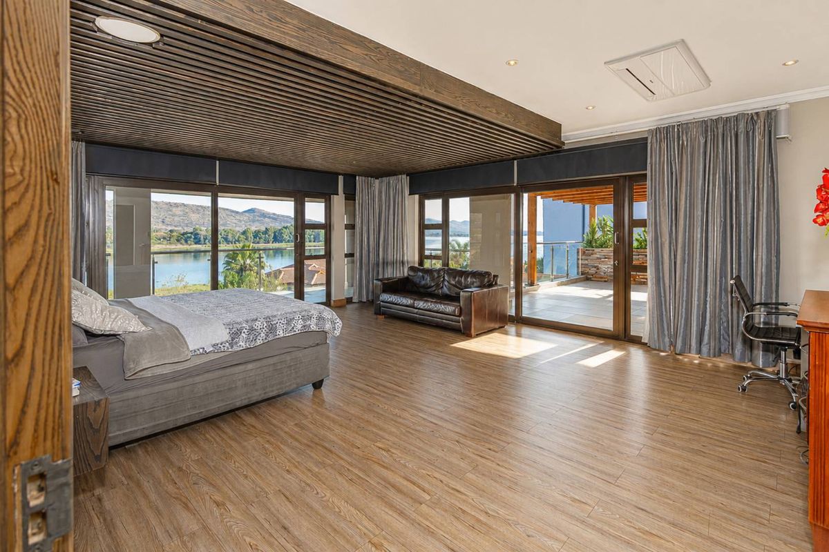 Spacious bedroom featuring wood-look flooring, a unique slatted timber ceiling, and large sliding glass doors opening onto a private balcony with scenic water views.
